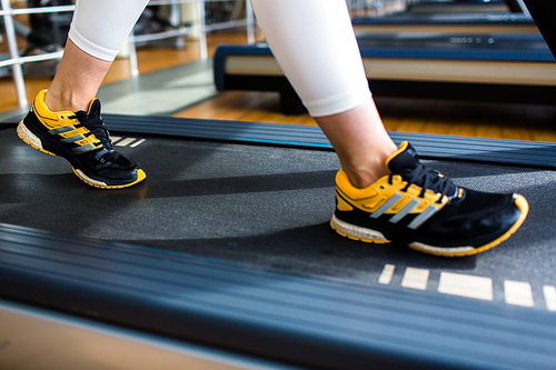 Human feet on threadmill moving track during workout in gym