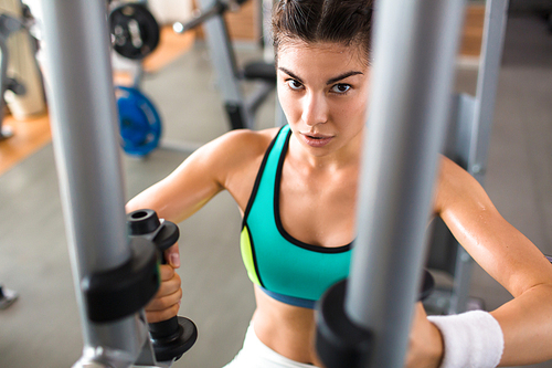 Confident athletic woman  while having intensive training on butterfly machine at modern gym, waist-up portrait