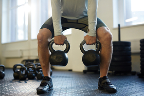 Low section portrait of unrecognizable man lifting two heavy kettlebells with vigorous effort during workout on gym