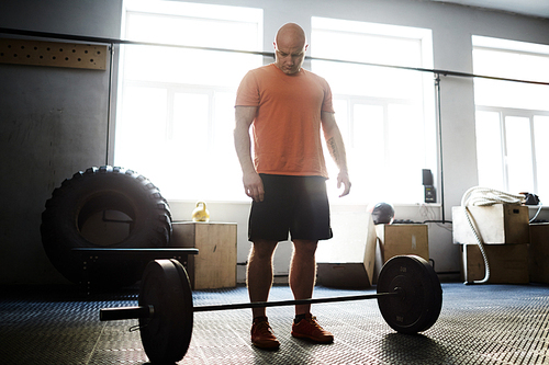 Middle-aged sporty man preparing for deadlift while having intensive training in gym, full-length portrait