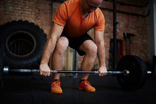 Bald professional athlete lifting barbell while working out in gym, full-length portrait