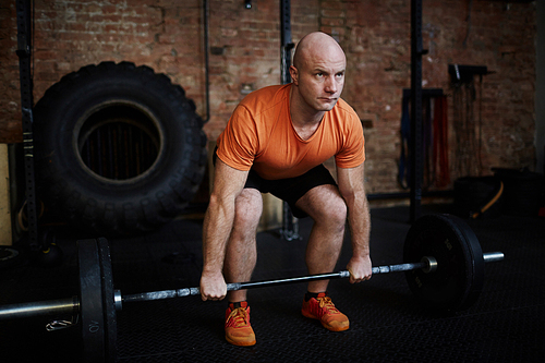 Middle-aged fit man working out with barbell in spacious gym, full-length portrait