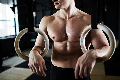 Motivational closeup shot of unrecognizable fit athlete with defined muscle pattern on chest and arms resting after exercising with gymnastic rings