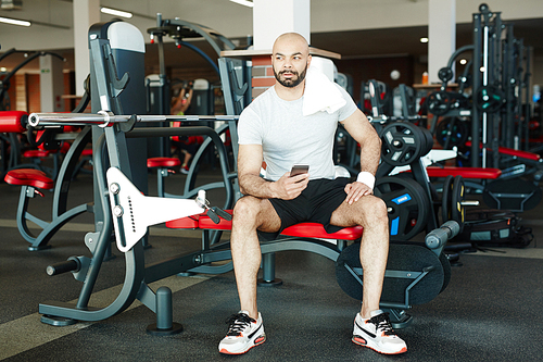Restful athlete with smartphone sitting in gym