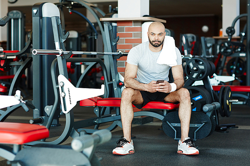 Young sporty man with smartphone sitting in gym