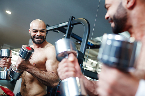Active man looking in mirror while exercising with dumbbells
