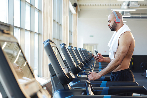 Man with headphones and smartphone messaging in gym