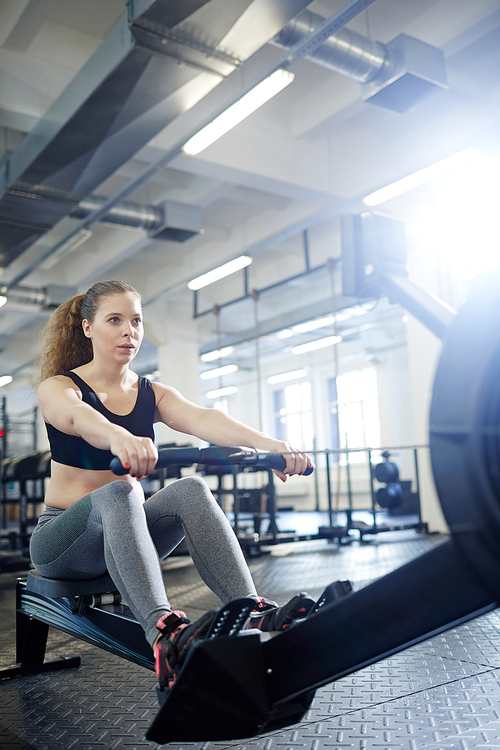 Young female sweating while rowing in gym