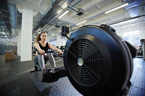 Fit girl training on rowing-machine in sport club