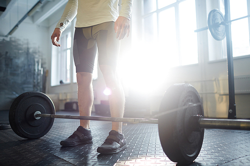 Athlete in sportswear standing by barbell in gym