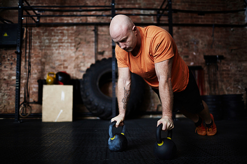 Middle-aged sportsman doing push-ups with kettlebells during intensive workout in modern gym, full-length portrait