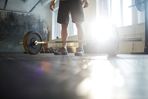 Low section of unrecognizable strong man ready to lift heavy barbell from floor during powerlifting workout in sunlit gym