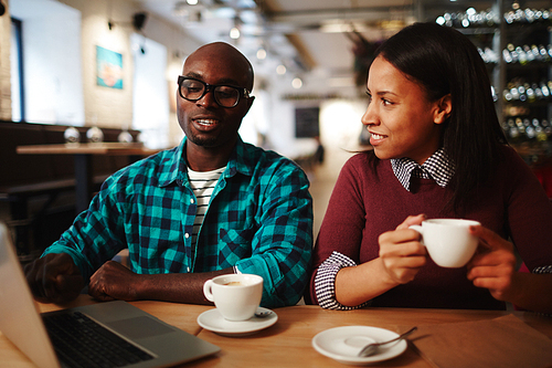 Two intercultural businesspeople having coffee in cafe and talking at meeting