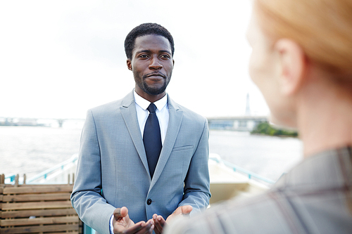 Over shoulder view of unrecognizable entrepreneur conducting negotiations with African American business partner while standing on upper deck of ship