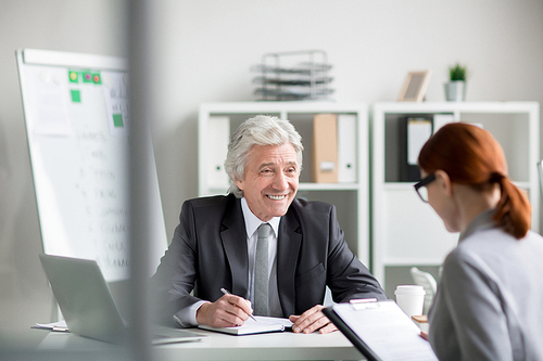 Happy senior employer having talk with young applicant during interview in his office