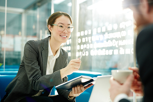 Pretty woman in formalwear discussing plans or project with colleague in office