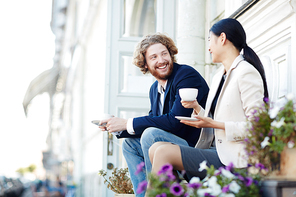 Young friendly colleagues with cups of coffee having talk at break in urban environment