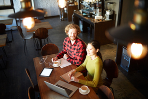 Young intercultural associates sitting in cafe in front of laptop and preparing new project