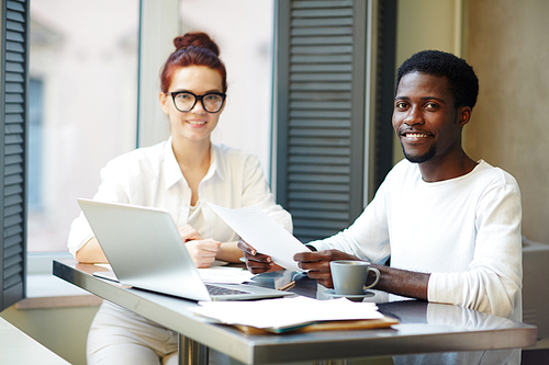 Multi-ethnic team of financial managers posing for photography while sitting at boardroom table and analyzing statistic data, group portrait