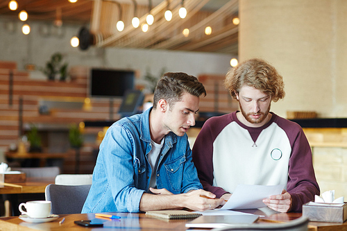 Group of talented financial managers analyzing results of accomplished work while having working meeting at cozy small coffeehouse, blurred background