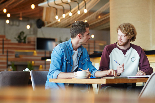 Friendly guys sitting in cafe and discussing homework or assignment for seminar