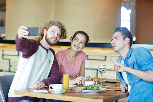 Cheerful friends sitting in cafe and making selfie by lunch