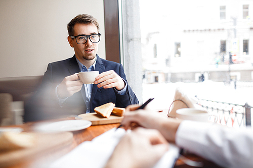 Young employee with cup of tea having talk with business partner