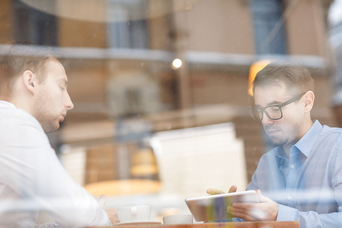 Businesman with touchpad working online in cafe with his colleague near by