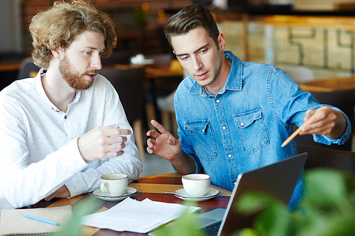 Group of young entrepreneurs gathered together at cozy coffeehouse and preparing for important negotiations with business partners, blurred background