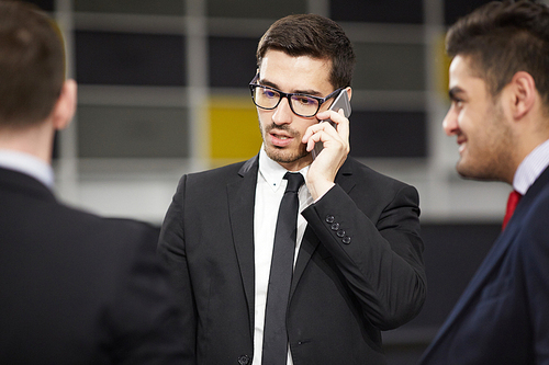 Ambitious professional speaking by smartphone with two colleagues near by