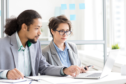 Young man and woman analyzing online information by workplace