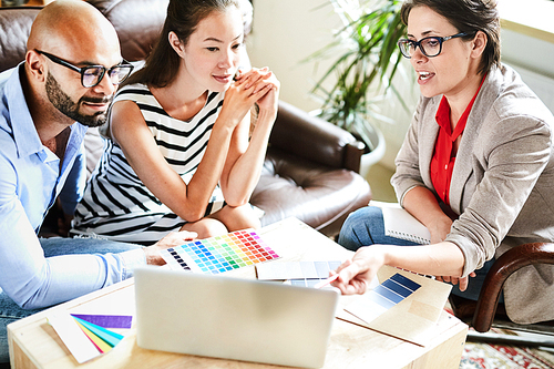 Pretty middle-aged interior designer sharing ideas with her clients while having meeting in cozy boardroom, they listening to her with interest