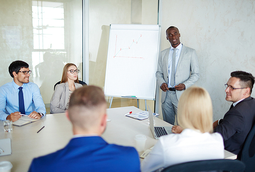 Multi-ethnic team of talented managers discussing growth strategy of their company while sitting in modern board room