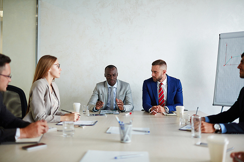 Colleagues attending work meeting: they gathered around table and listening to their Afro-American boss with concentration