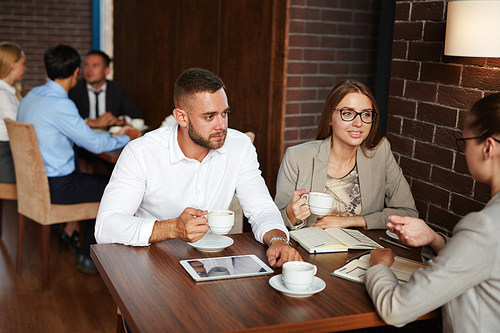 Young white collar workers enjoying fragrant coffee while their colleague entertaining them with small talk in lovely coffeehouse