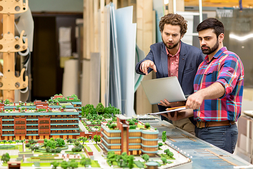 Two architects pointing at one of buildings on layout model of the city during discussion