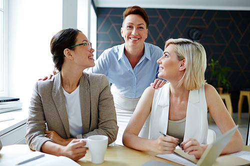 Two smiling females looking at their successful employer and leader of team