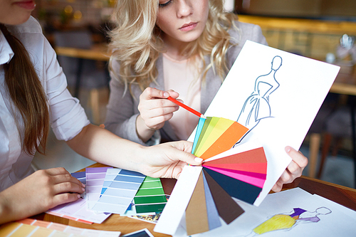 Two fashion designers choosing color for new model of dress from pantone chart