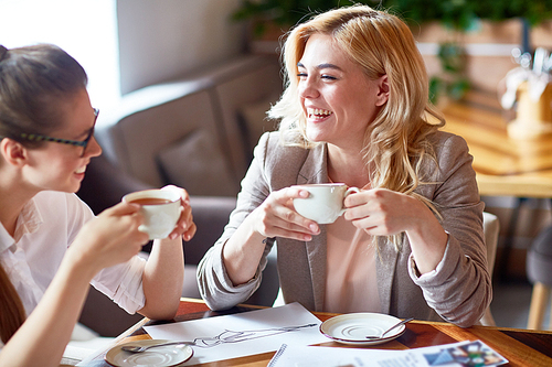 Two laughing girls having tea and discussing new creative project in cafe