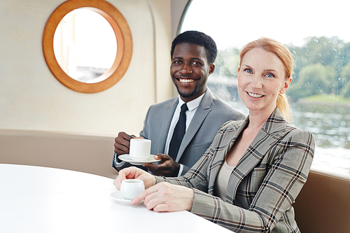 Cheerful co-workers or business leaders with cups of tea or coffee having nice time in steamship cafe