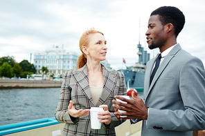 Two professionals with drinks talking on steamship by waterside