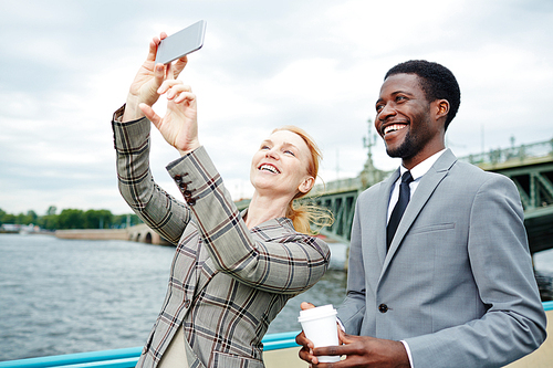 Laughing colleagues making selfie during business travel by water