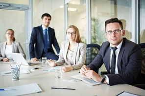 Waist-up portrait of serious middle-aged businessman in eyeglasses  with concentration while having board meeting