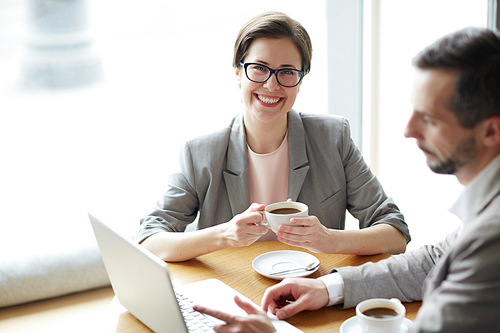 Happy young businesswoman with cup of tea  with co-worker sitting near by