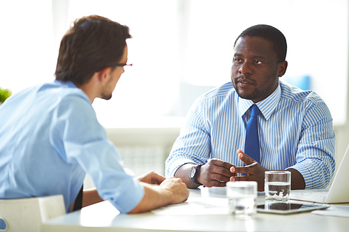 Portrait of confident middle-aged businessman holding negotiations with his partner while sitting in boardroom