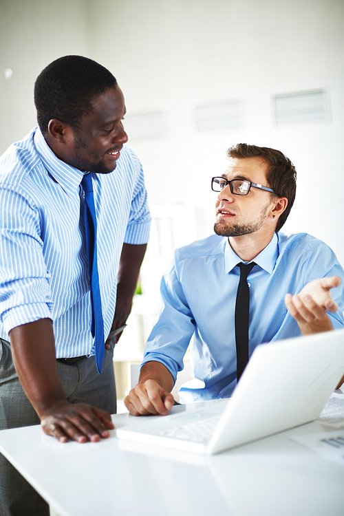 Bearded employee with eyeglasses sitting at office desk and showing results of accomplished work to his middle-aged superior