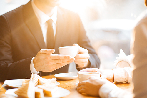 Hands of modern banker with cup of coffee during talk with colleague