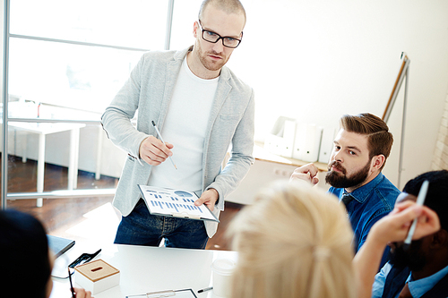 Multiethnic group of managers sharing ideas at meeting, handsome team leader in eyeglasses standing at table and listening to his female colleague with interest