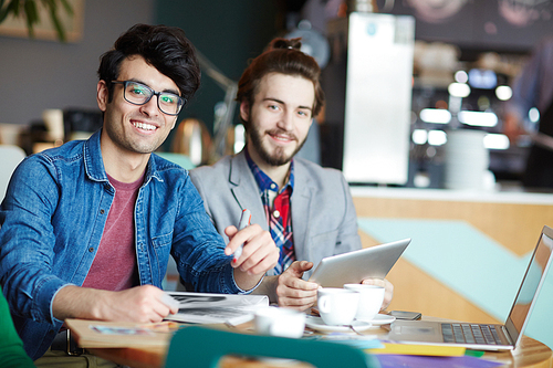Portrait of two creative young men dressed in business casual smiling  while working at table during meeting