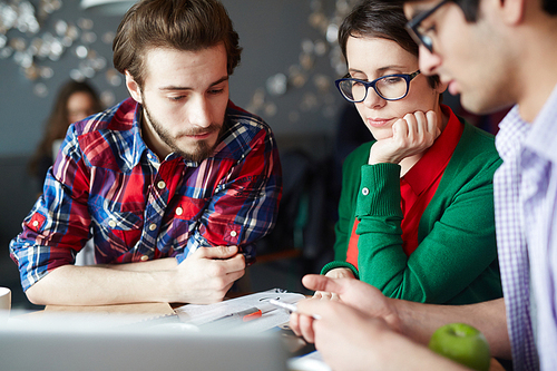 Group of young creative people wearing business casual clothes collaborating at meeting table and discussing work